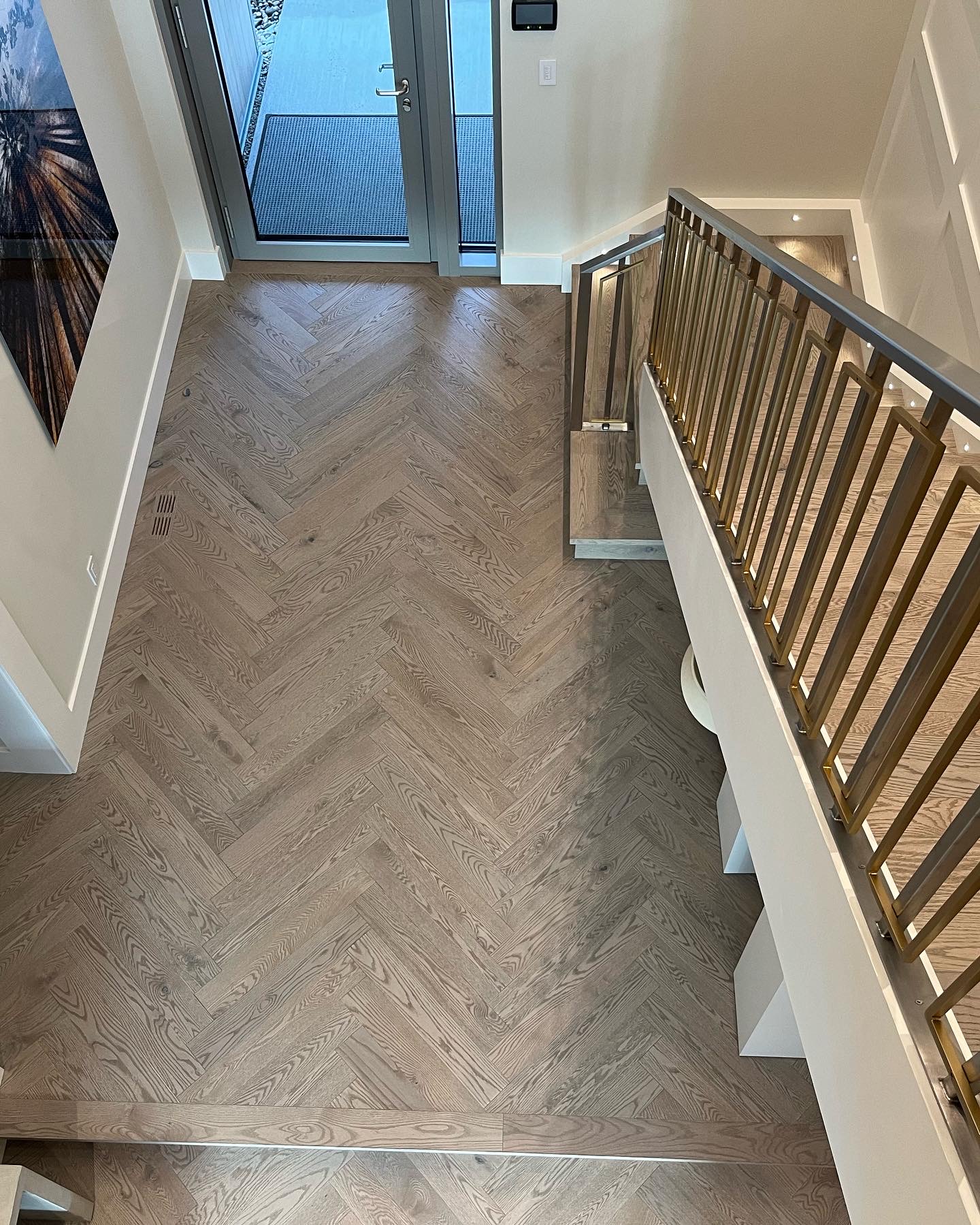 Whistler Home — overhead view of white oak herringbone entry beside brass and metal staircase