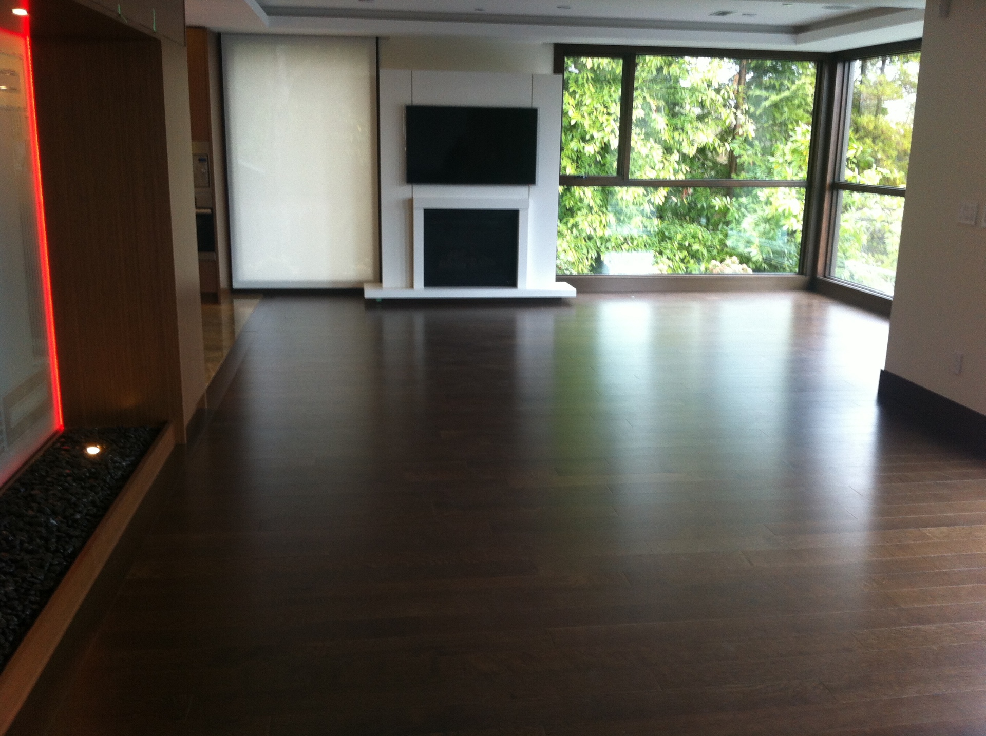 West Vancouver Home — Vintage walnut hardwood in open living area with fireplace, mounted TV and forest-view windows