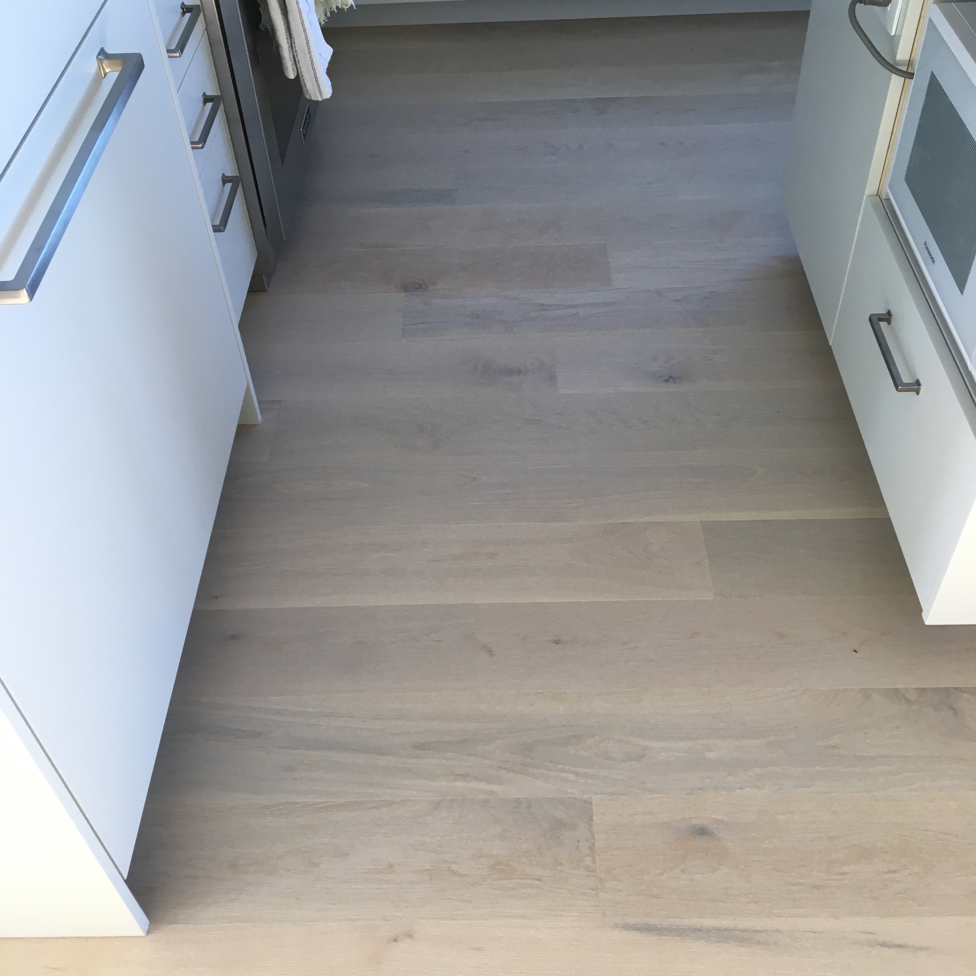 Point Grey Rd Vancouver Home — Mirage white oak hardwood in white kitchen between appliances