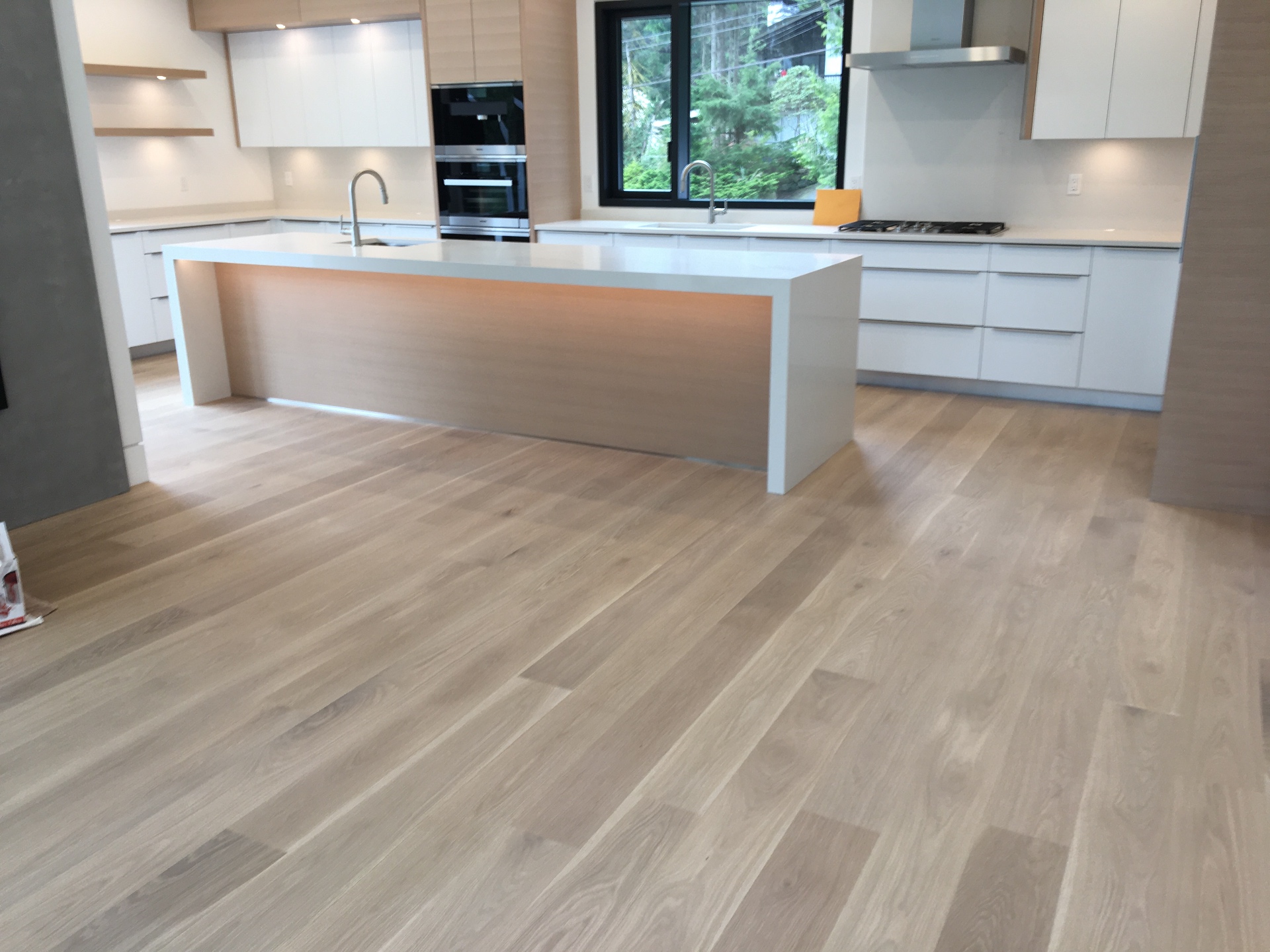 West Vancouver Home — site-sanded white oak hardwood in modern white kitchen with waterfall island
